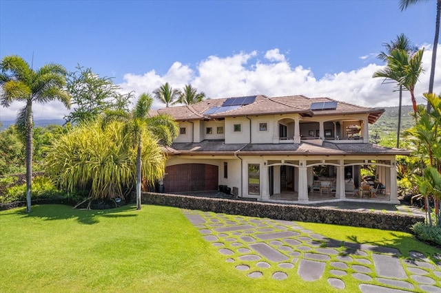 back of property with a garage, solar panels, a lawn, and a patio