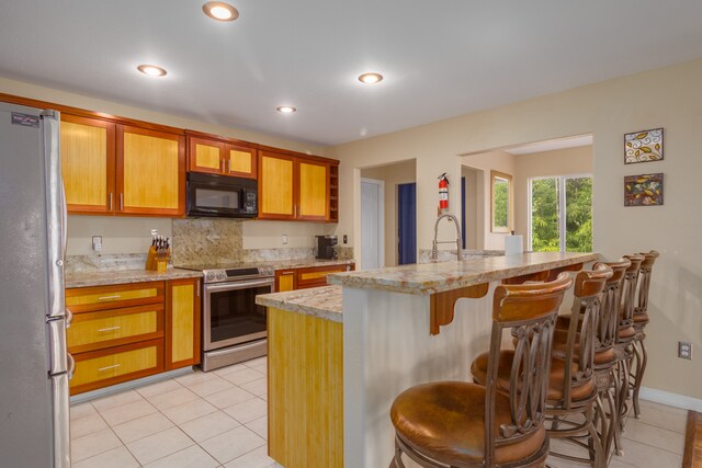 kitchen featuring a kitchen bar, light stone countertops, stainless steel appliances, light tile patterned floors, and a center island with sink