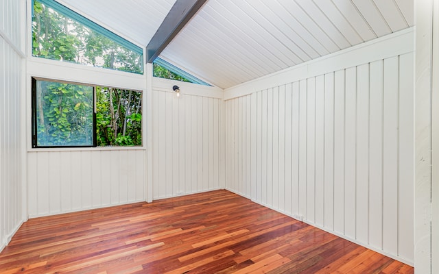 empty room featuring vaulted ceiling with beams, hardwood / wood-style flooring, and wood walls