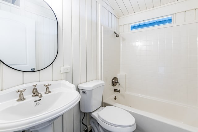 full bathroom with sink, wood walls, toilet, and washtub / shower combination