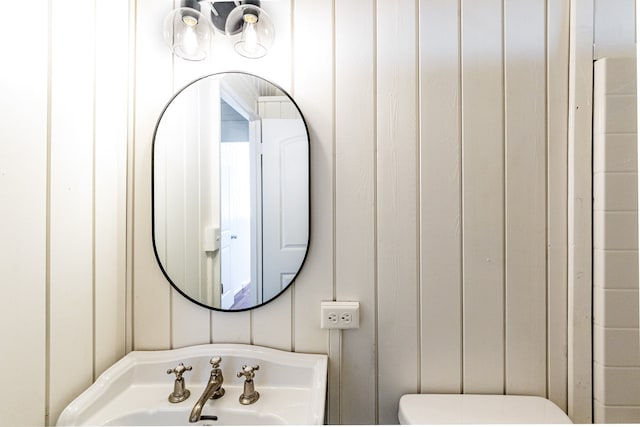 bathroom with wood walls, toilet, and sink