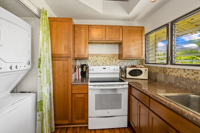 kitchen with white appliances, dark wood-type flooring, stacked washer / drying machine, a textured ceiling, and dark stone counters