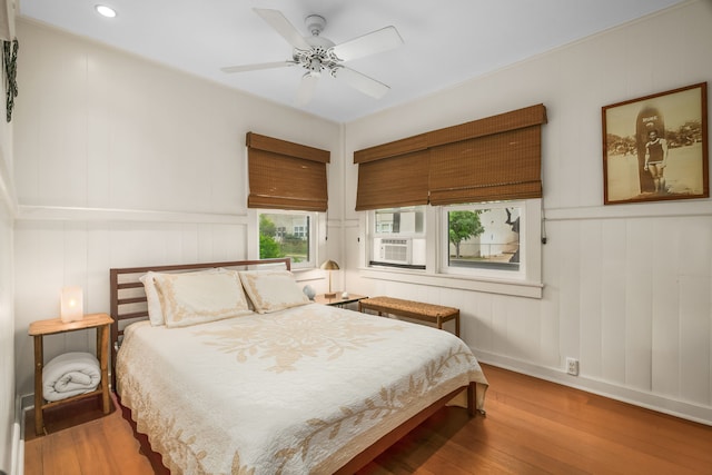 bedroom with wood finished floors, cooling unit, a decorative wall, recessed lighting, and baseboards