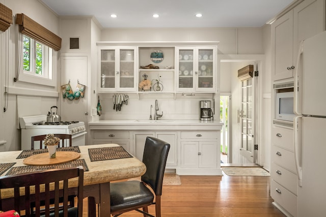 kitchen featuring white appliances, light wood finished floors, a sink, white cabinets, and recessed lighting
