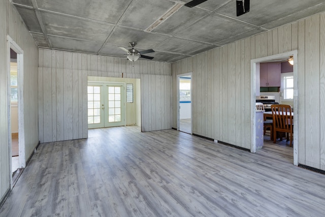 spare room featuring a healthy amount of sunlight, light hardwood / wood-style floors, wooden walls, and ceiling fan