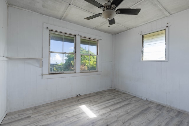 unfurnished room with light hardwood / wood-style flooring, wooden walls, and ceiling fan