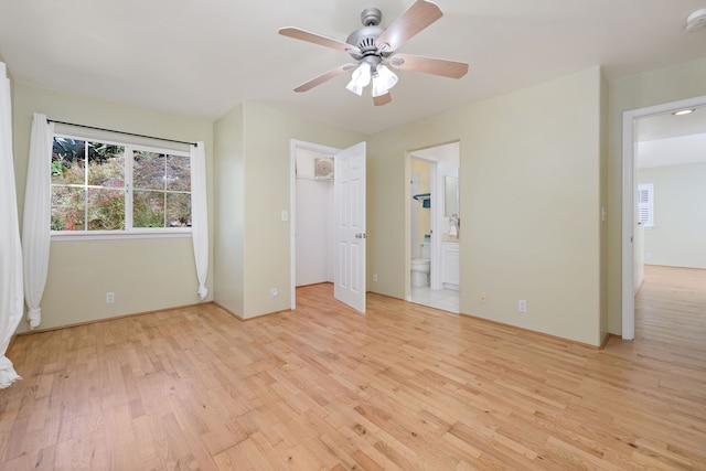 unfurnished bedroom with ceiling fan, ensuite bathroom, light hardwood / wood-style floors, and a walk in closet