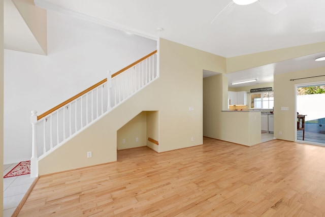 unfurnished living room with a towering ceiling, light wood-type flooring, and ceiling fan