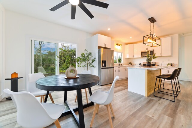 interior space featuring appliances with stainless steel finishes, a kitchen island, light hardwood / wood-style floors, white cabinetry, and hanging light fixtures