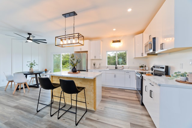 kitchen featuring pendant lighting, white cabinets, light hardwood / wood-style floors, a kitchen island, and stainless steel appliances