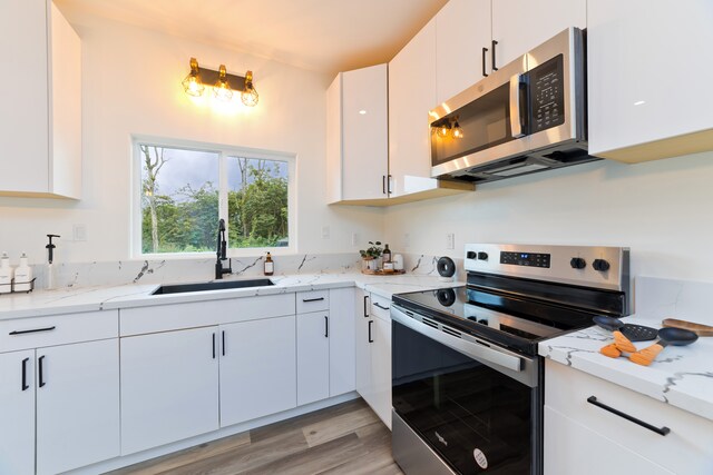 kitchen featuring appliances with stainless steel finishes, light stone counters, sink, light hardwood / wood-style flooring, and white cabinetry