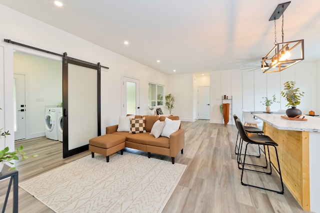 living room with washer and dryer, light hardwood / wood-style floors, a barn door, and an inviting chandelier