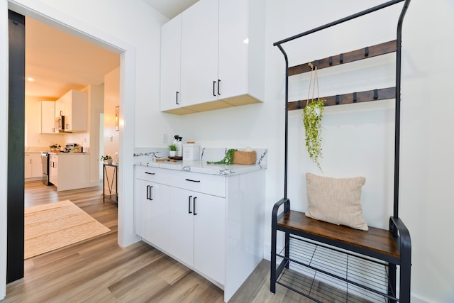 bar with white cabinetry, stainless steel appliances, and light wood-type flooring