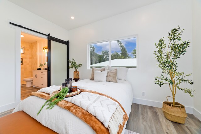 bedroom with connected bathroom, hardwood / wood-style flooring, and a barn door