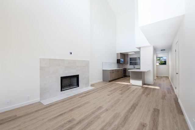 unfurnished living room featuring a high ceiling, a tile fireplace, and light hardwood / wood-style floors