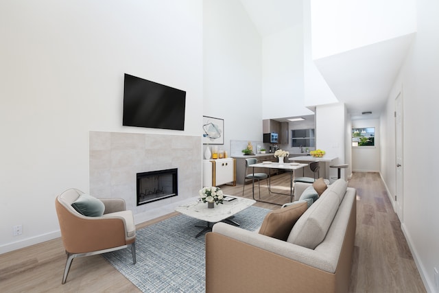 living room featuring a towering ceiling, a tiled fireplace, and light hardwood / wood-style floors