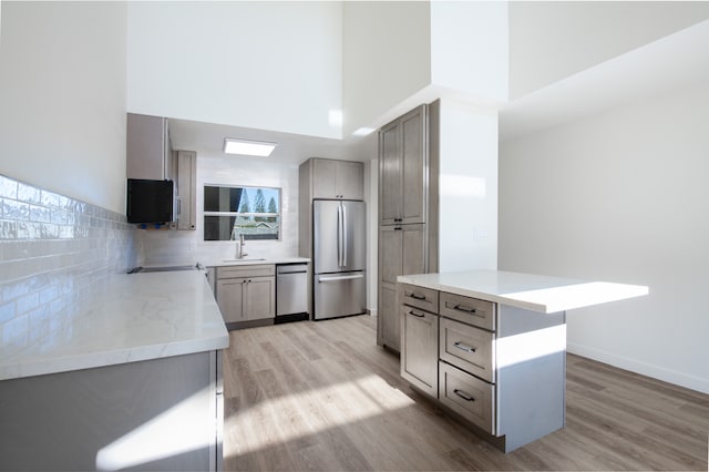 kitchen with tasteful backsplash, a kitchen island, light hardwood / wood-style flooring, stainless steel appliances, and a towering ceiling