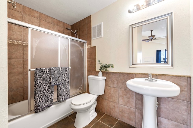 bathroom featuring tile walls, tile patterned flooring, shower / bath combination with glass door, ceiling fan, and toilet