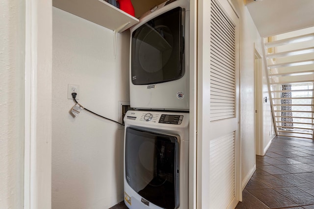 clothes washing area featuring dark tile patterned flooring and stacked washing maching and dryer