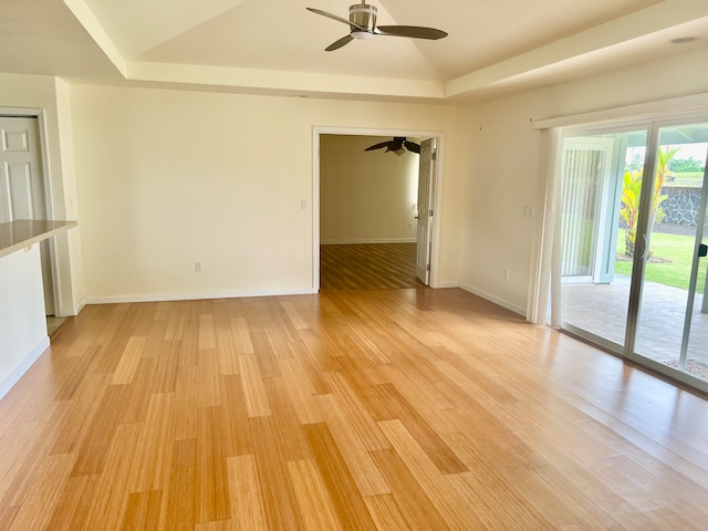 empty room with light hardwood / wood-style floors, ceiling fan, and a raised ceiling