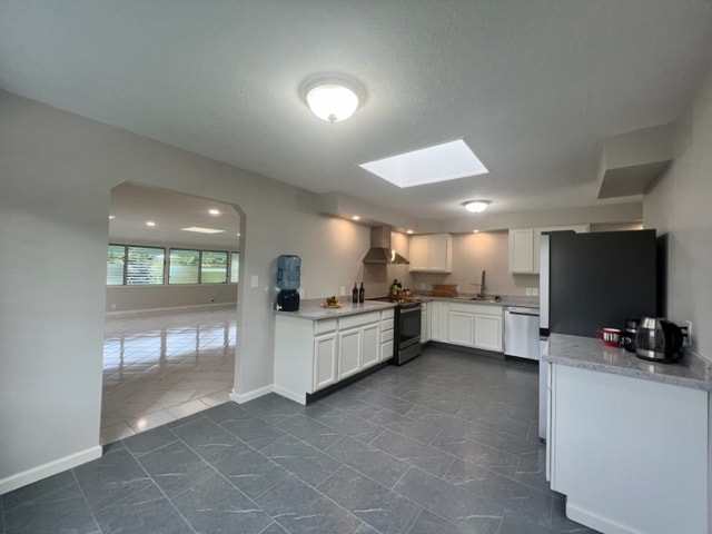 kitchen with a skylight, wall chimney exhaust hood, white cabinetry, dishwasher, and black range with electric cooktop