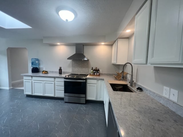 kitchen featuring sink, white cabinetry, wall chimney range hood, a skylight, and appliances with stainless steel finishes