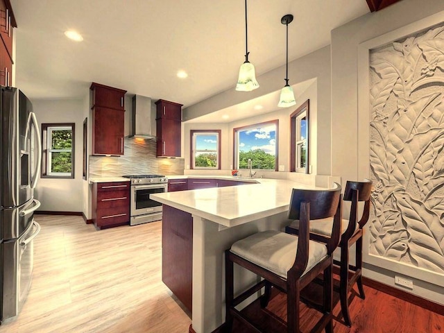 kitchen with appliances with stainless steel finishes, kitchen peninsula, light wood-type flooring, a kitchen bar, and decorative light fixtures