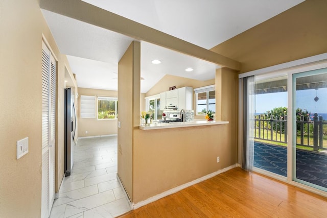 kitchen with kitchen peninsula, appliances with stainless steel finishes, white cabinetry, light wood-type flooring, and vaulted ceiling