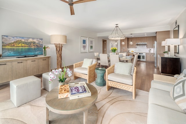 living room with ceiling fan with notable chandelier and light hardwood / wood-style floors