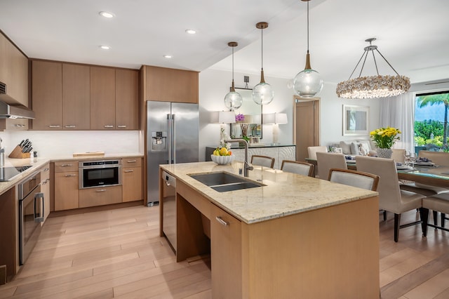 kitchen featuring stainless steel appliances, hanging light fixtures, sink, and light hardwood / wood-style flooring