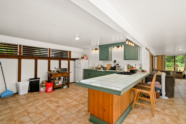 kitchen with stainless steel gas cooktop, tile countertops, green cabinets, kitchen peninsula, and white refrigerator