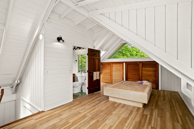 bedroom with beam ceiling, hardwood / wood-style flooring, high vaulted ceiling, ensuite bathroom, and wooden walls