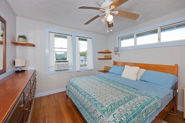 bedroom featuring dark hardwood / wood-style floors, cooling unit, ceiling fan, a textured ceiling, and wood walls