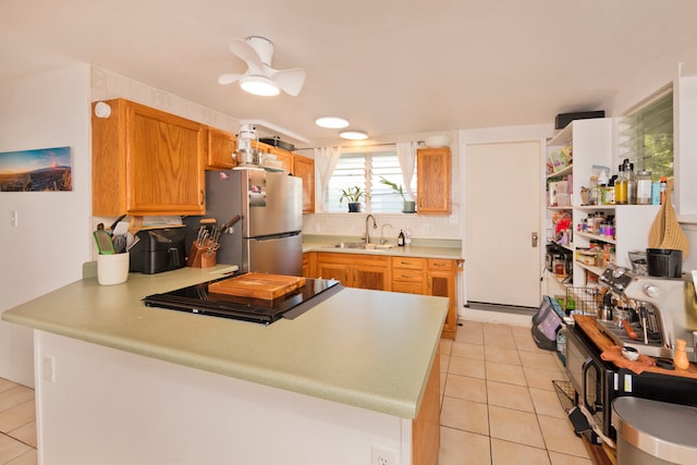 kitchen featuring kitchen peninsula, sink, light tile patterned floors, and stainless steel refrigerator