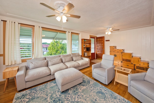 living room featuring ceiling fan, a textured ceiling, ornamental molding, and light wood-type flooring