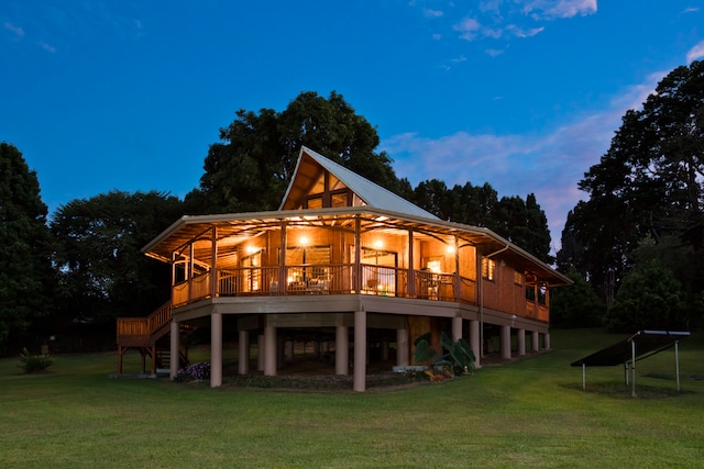 back house at dusk featuring a wooden deck and a lawn