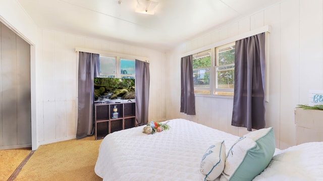 bedroom featuring wood walls, multiple windows, and light carpet