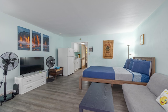 bedroom featuring freestanding refrigerator, connected bathroom, and wood finished floors