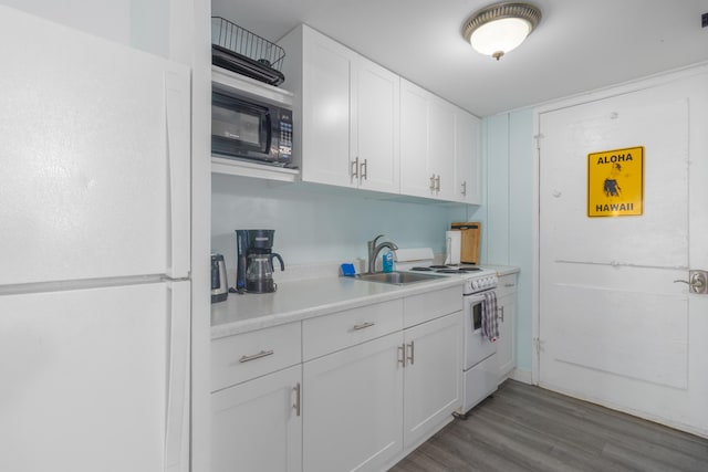 kitchen featuring white appliances, light countertops, white cabinets, a sink, and wood finished floors