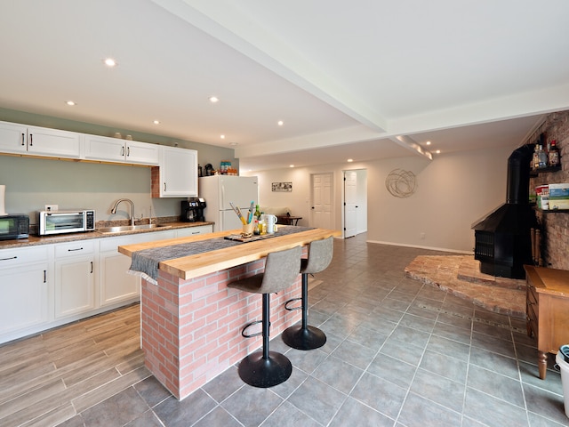 kitchen with white cabinets, white refrigerator, sink, a breakfast bar, and wood counters