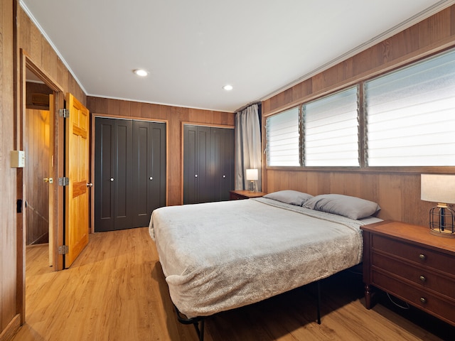 bedroom featuring light hardwood / wood-style floors, wooden walls, and two closets