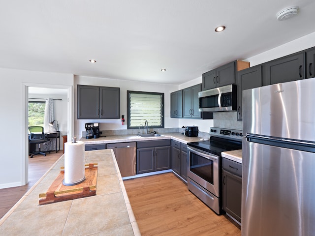 kitchen featuring tile counters, appliances with stainless steel finishes, light wood-type flooring, and sink