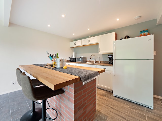 kitchen with a breakfast bar, white cabinets, white fridge, wood-type flooring, and sink