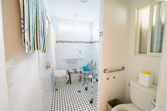 bathroom with tile walls, a tile shower, tile patterned floors, and toilet