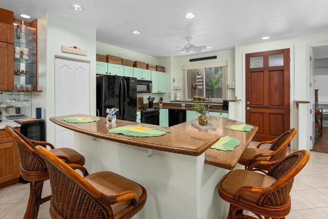 kitchen with ceiling fan, dark stone countertops, a kitchen bar, light tile patterned flooring, and black appliances