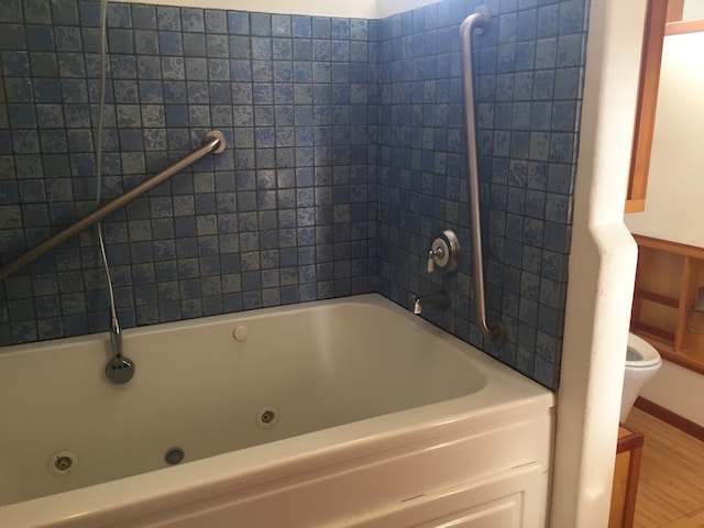 bathroom with wood-type flooring, a tub to relax in, and toilet