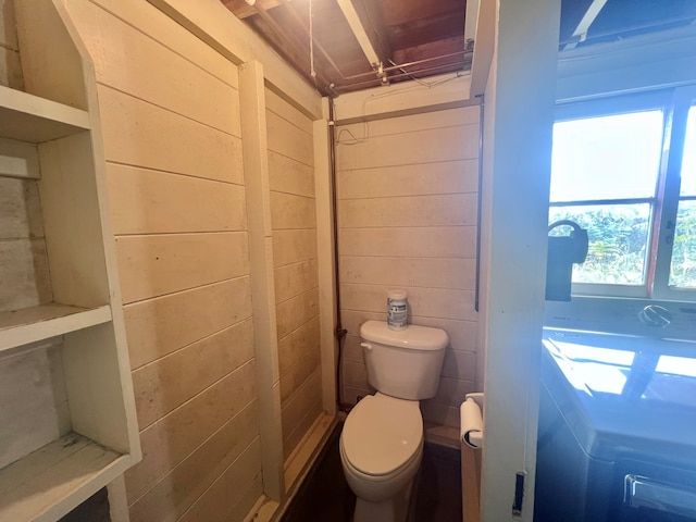 bathroom with toilet, washer / clothes dryer, and wooden walls