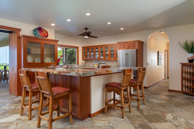 kitchen featuring kitchen peninsula, a kitchen bar, backsplash, ceiling fan, and stainless steel fridge