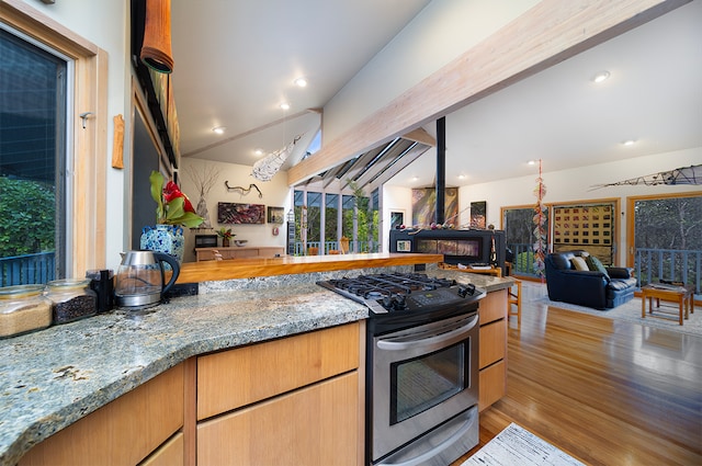 kitchen featuring light wood-type flooring, light stone counters, gas stove, a fireplace, and vaulted ceiling