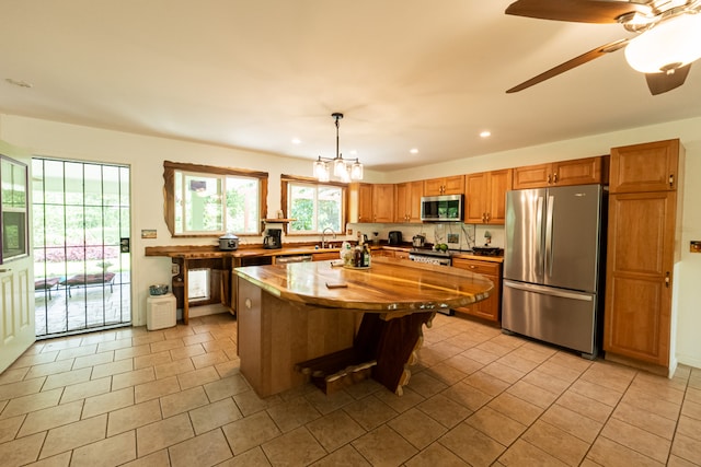 kitchen featuring hanging light fixtures, stainless steel appliances, a center island, ceiling fan, and sink